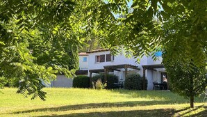 A house with a covered patio, a lawn, and a tree in the foreground. - Lovely Duplex Near Historic Carayac (Carayac)