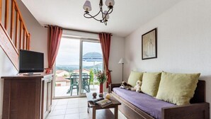 A room with a sofa, a TV, a table with books, a lamp, and a view of the outdoors. - Lovely Duplex Near Historic Carayac (Carayac)