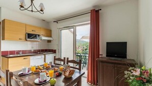 A kitchen with a microwave, dining table with breakfast, and a TV on a cabinet. - Lovely Duplex Near Historic Carayac (Carayac)