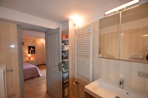 Ein Badezimmer mit Waschbecken, Spiegel, Handtuchhalter und Duschbereich.