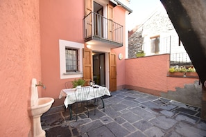 Eine Terrasse mit Steinboden, einem Tisch, Stühlen, einem Spülbecken und einem Balkon mit Geländer.