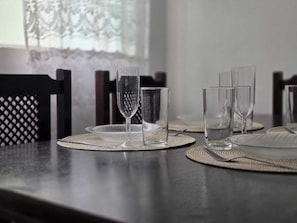 A dining table with clear glassware and plates, set with woven placemats.