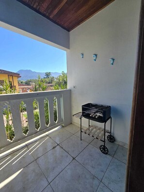 A balcony with a barbecue grill, a view of mountains, and a tiled floor.