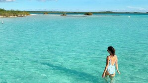 A woman in a swimsuit standing in clear turquoise water. - HEADLINE CAMPER 1 (Bacalar)