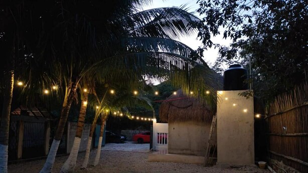 A pathway leading to a building with a thatched roof, surrounded by palm trees and a fence. - HEADLINE CAMPER 1 (Bacalar)