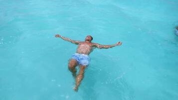 A person floating in clear turquoise water with arms outstretched.
