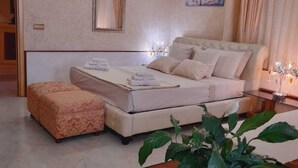 A bedroom with a bed, a bedside table, a mirror, and a potted plant.