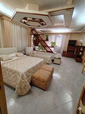 Ein geräumiges Schlafzimmer mit einem großen Bett, einem kleineren Bett, einer Couch, einem Sessel und einer Holztreppe.