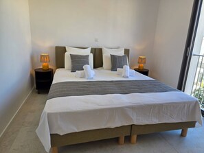 Ein ordentlich bezogenes Bett mit Kissen und Decke, zwei Nachttische und ein Blick ins Freie.