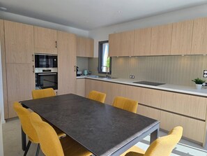 Eine moderne Küche mit Holzschränken, einem Einbauofen, einer Spüle und einem Essbereich mit Tisch und Stühlen.