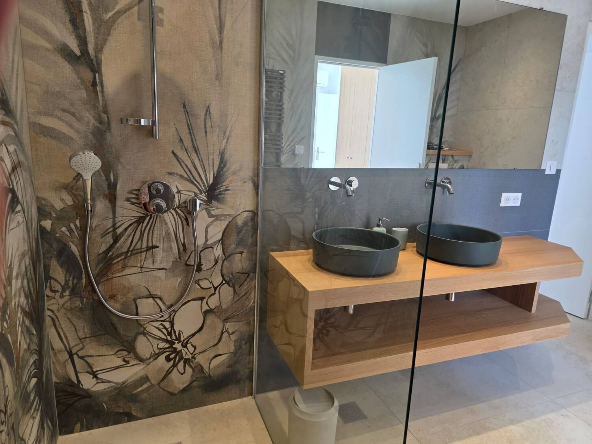 Une salle de bain moderne avec un meuble-lavabo en bois, deux vasques noires, une cabine de douche en verre et un grand miroir.