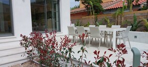 Eine Terrasse mit weißen Tischen und Stühlen, umgeben von Pflanzen mit roten Blättern.
