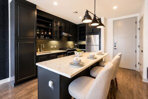 A modern kitchen with dark cabinetry, a stainless steel refrigerator, a central island with seating, and pendant lighting.