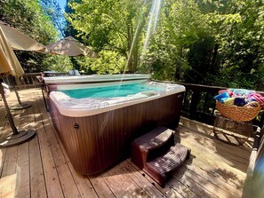 Una vasca idromassaggio su un pontile di legno, circondata da alberi.
