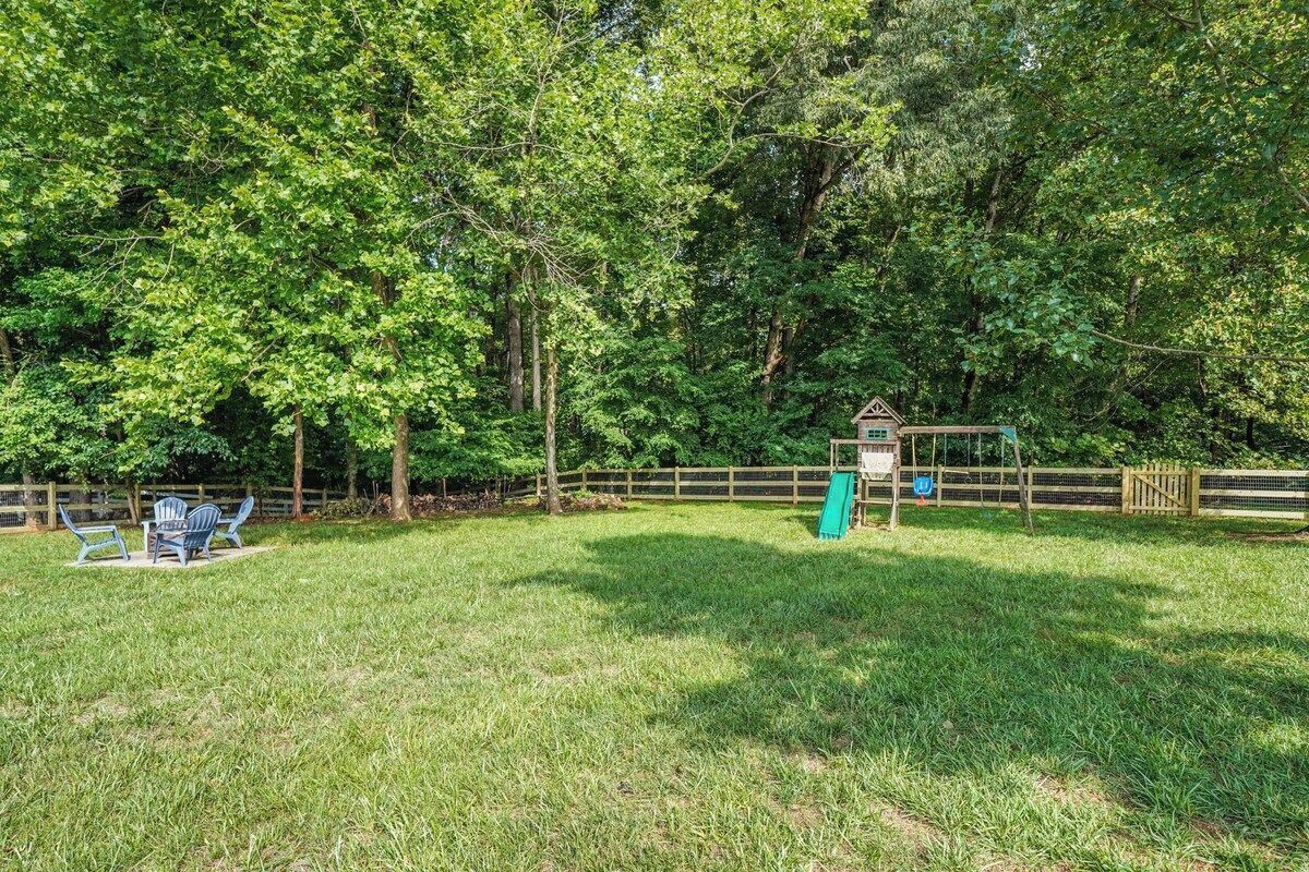 A grassy outdoor area with a wooden fence, a small structure, and a table with chairs.