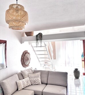 A modern living room with a curved sofa, a woven pendant light, a staircase, and a large window. - Grace House - Spacious Villa in a Prime Location Between Castelsardo and Alghero (Arboriamar)