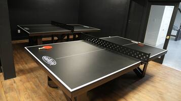 Une pièce équipée de tables de ping-pong, dotée d’un plancher en bois et d’une porte donnant accès à un autre espace.