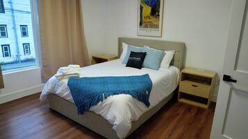 Un lit bien fait, avec une couverture bleue, un coussin orné d’un motif et une œuvre d’art encadrée accrochée au mur.