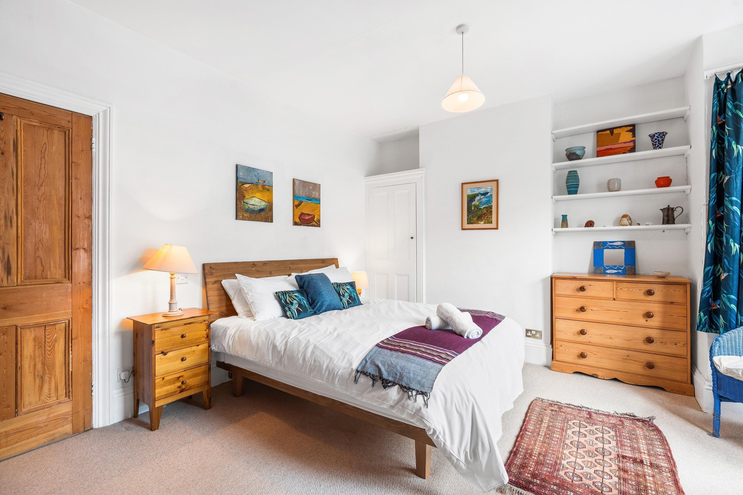 Ein Schlafzimmer mit einem hölzernen Bett, Nachttischen, einem Schminktisch und Wandbildern.