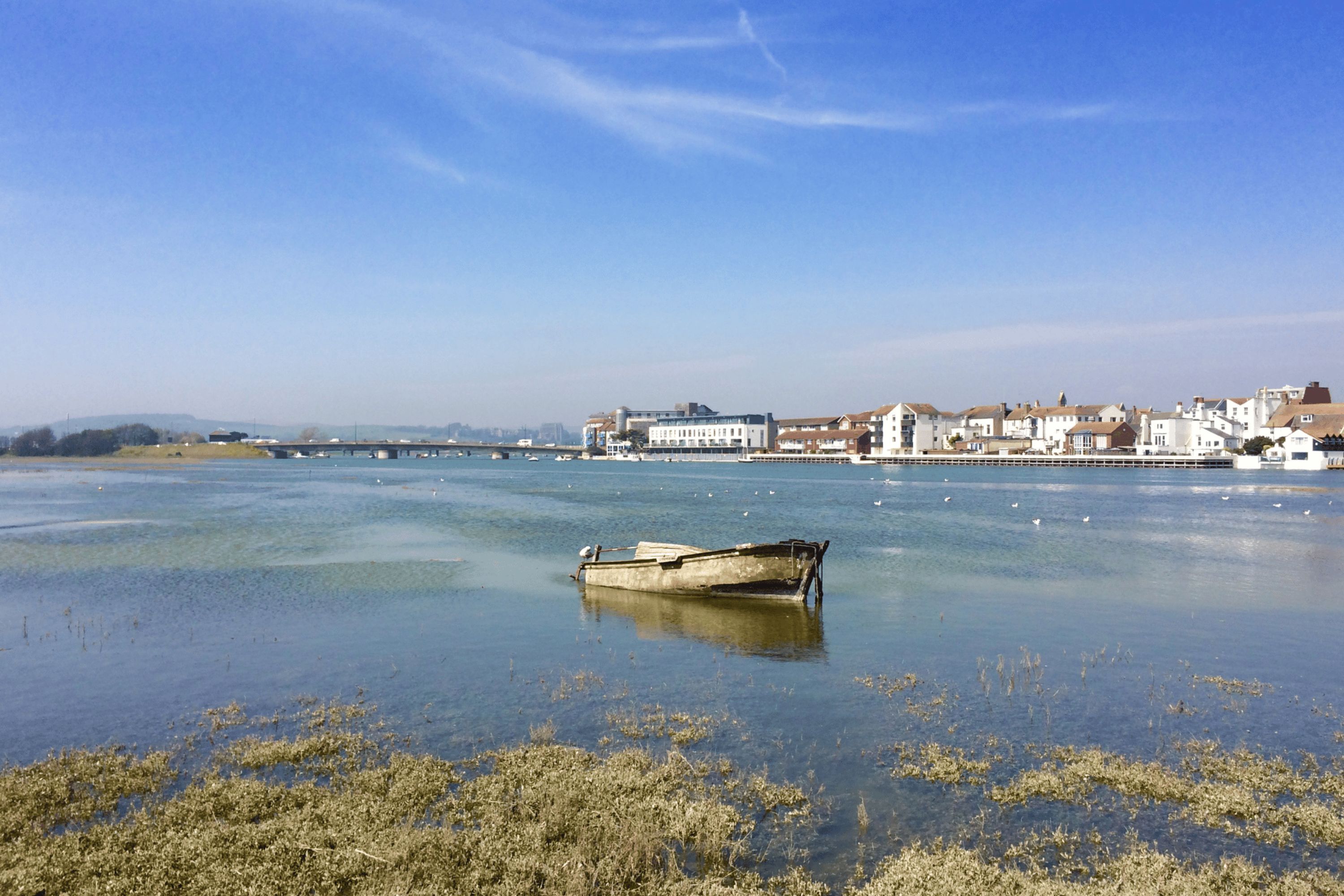 Un río tranquilo con una pequeña embarcación, edificios a lo largo de la orilla y un cielo despejado.