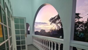 A balcony with a view of the sunset, a white railing, and a door with glass panels. - Cozzy Villa Rans Cimacan (cianjur)