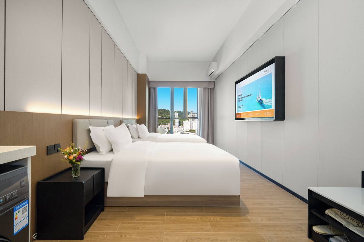 A modern hotel room with a large bed, a TV on the wall, and a view of the city.