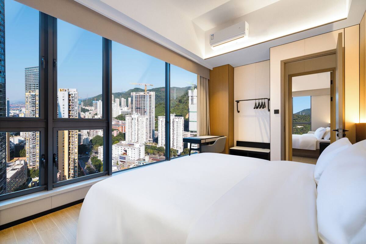 A hotel room with a large window, a bed, a desk, and a chair.