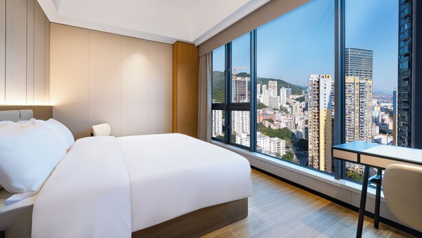 A hotel room with a large bed, a desk, and a view of a cityscape through large windows. - YEENFON HOTEL (Shenzhen)