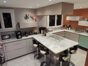 A modern kitchen with a central island, bar stools, a coffee station, and decorative items. - 3-bedroom single-family home, 3 km from the beaches and close to everything: restaurants, movie theater, park, and sports facilities (La Garde)