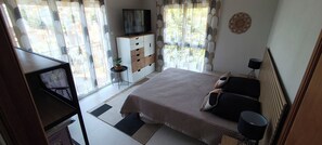 A bedroom with a bed, bedside tables, a TV, a small table with a plant, and a window with curtains. - 3-bedroom single-family home, 3 km from the beaches and close to everything: restaurants, movie theater, park, and sports facilities (La Garde)