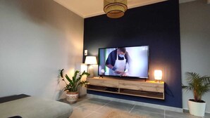 A modern living room with a flat-screen TV, a sofa, two potted plants, and a wooden console table. - 3-bedroom single-family home, 3 km from the beaches and close to everything: restaurants, movie theater, park, and sports facilities (La Garde)