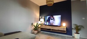 A modern living room with a flat-screen TV, a sofa, two potted plants, and a wooden console table. - 3-bedroom single-family home, 3 km from the beaches and close to everything: restaurants, movie theater, park, and sports facilities (La Garde)