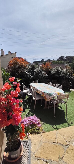 A patio with a table and chairs, surrounded by potted plants and flowers. - 3-bedroom single-family home, 3 km from the beaches and close to everything: restaurants, movie theater, park, and sports facilities (La Garde)