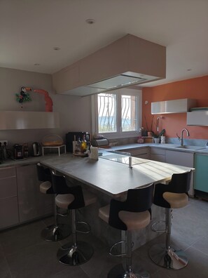 A modern kitchen with a central island, bar stools, a large window, and a view of the outdoors. - 3-bedroom single-family home, 3 km from the beaches and close to everything: restaurants, movie theater, park, and sports facilities (La Garde)