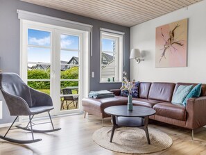 Ein Wohnzimmer mit einer Ledersofa, einem Schaukelstuhl, einem runden Couchtisch und Blick durch große Schiebetüren.
