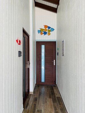 Ein Korridor mit einer Holztür, einem Wandbild mit Fischen, einem roten Schild und einem Thermostat.