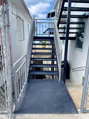 Eine Metalltreppe führt zu einem Gebäude, links daneben ein Metallgeländer und ein Metallzaun.