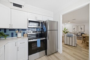 A modern kitchen with white cabinets, stainless steel appliances, and a blue-tiled backsplash. - Steps to Beach | Family Retreat w/ Community Pool (Indian Shores)