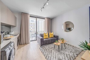 Eine moderne Wohnung mit Küche, grauem Sofa, kleinem runden Tisch und einem Balkon mit Vorhängen.