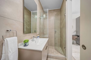 Ein modernes Badezimmer mit einer begehbaren Glasdusche, einem weißen Waschbecken mit einer Vase und einem Spiegel darüber.