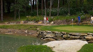 Un campo de golf con un estanque, muros de piedra y un marcador de bandera.