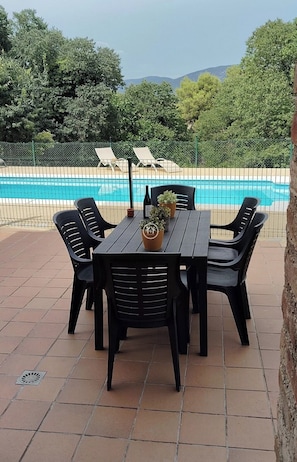 A patio with a pool, surrounded by a fence, and a table with chairs.