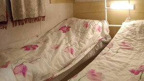Quarto individual com uma cama e cabeceira de madeira, uma janela com persiana branca e cortina.