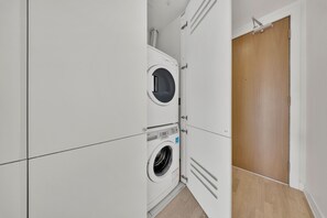 Ein kleiner Hauswirtschaftsraum mit einer Waschmaschine und einem Trockner mit Frontlader, einer Holztür und einem gefliesten Boden.