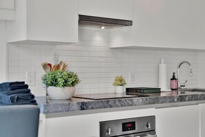 Une cuisine moderne avec des meubles blancs, un plan de travail en granit, une cuisinière intégrée et une petite plante en pot.