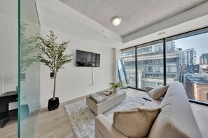 Ein modernes Wohnzimmer mit großem Fenster, Flachbildfernseher, einer Couch und einem Topf mit Pflanze.