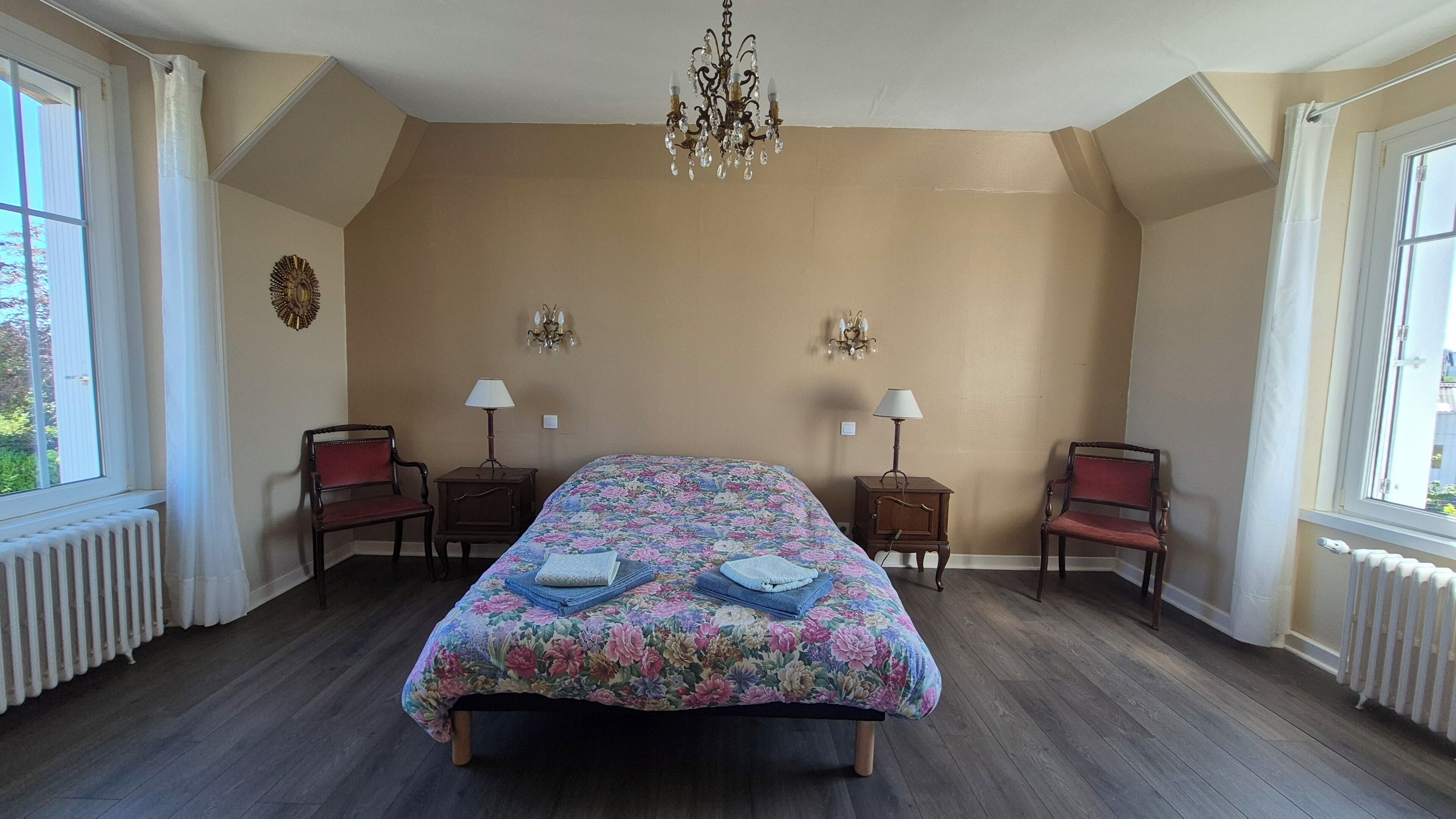A bedroom with a large bed, two bedside tables with lamps, a chandelier, and a radiator.