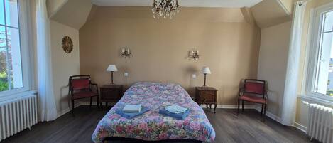 A bedroom with a large bed, two bedside tables with lamps, a chandelier, and a radiator.