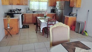 Une cuisine avec des meubles de rangement en bois, une table à manger avec des chaises, un réfrigérateur et une machine à café.