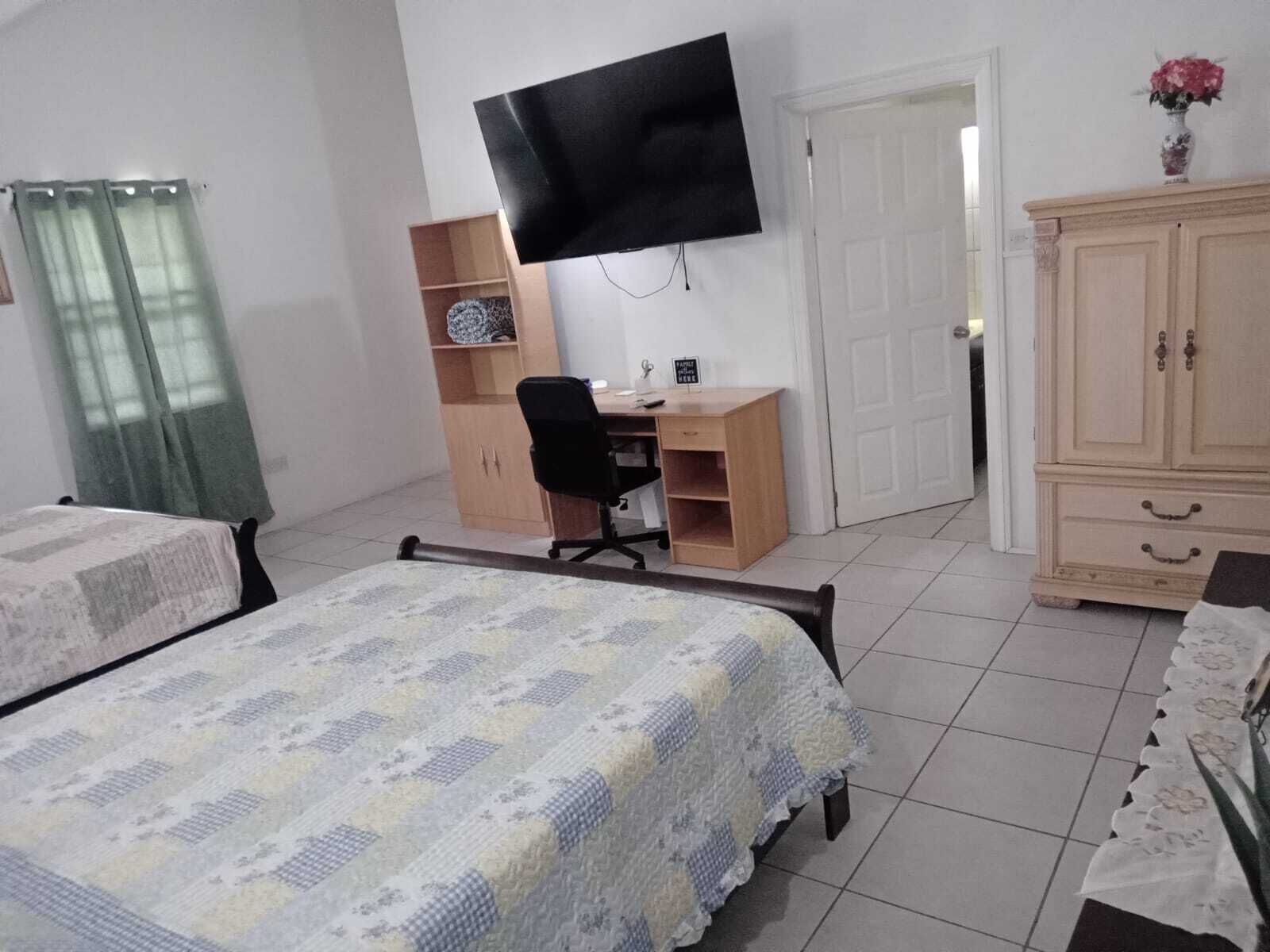 A bedroom with two beds, a desk, a chair, a television, and a wardrobe.